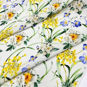 May include: White fabric with a floral print featuring white flowers with yellow centers, blue flowers, and yellow flowers with green leaves.