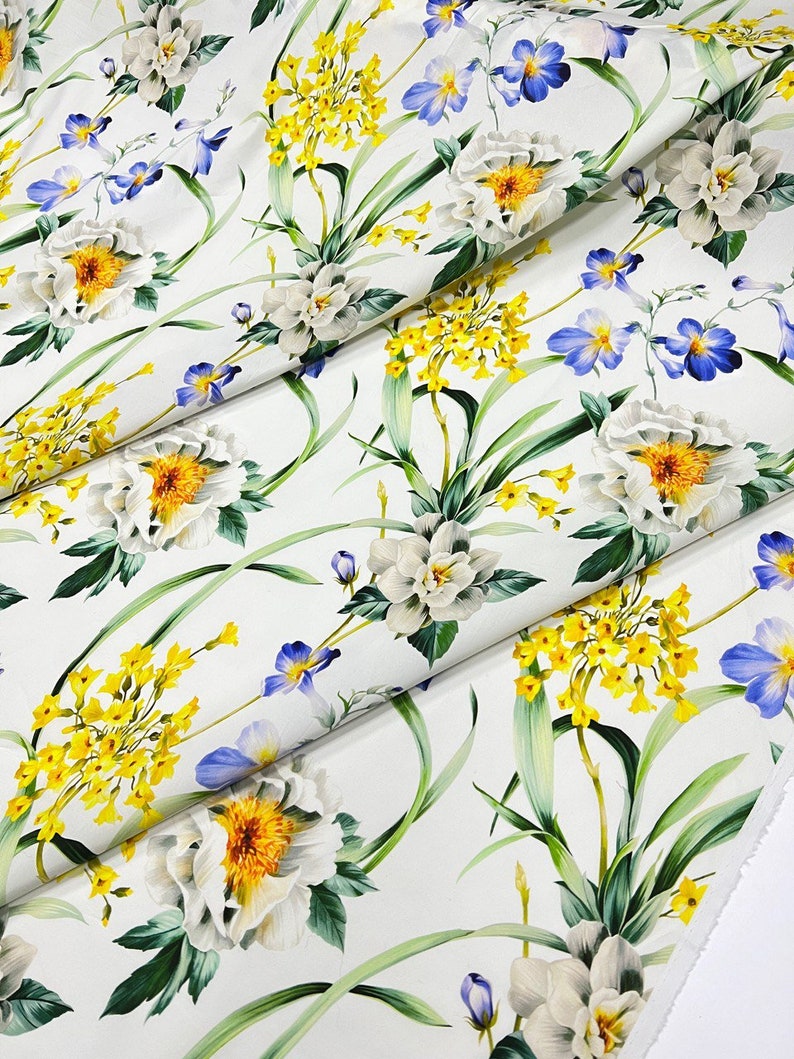 May include: White fabric with a floral print featuring white flowers with yellow centers, blue flowers, and yellow flowers with green leaves.