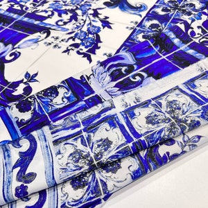 May include: Blue and white patterned fabric with a design of stylized flowers and vases. The fabric is folded and shows the pattern repeating.