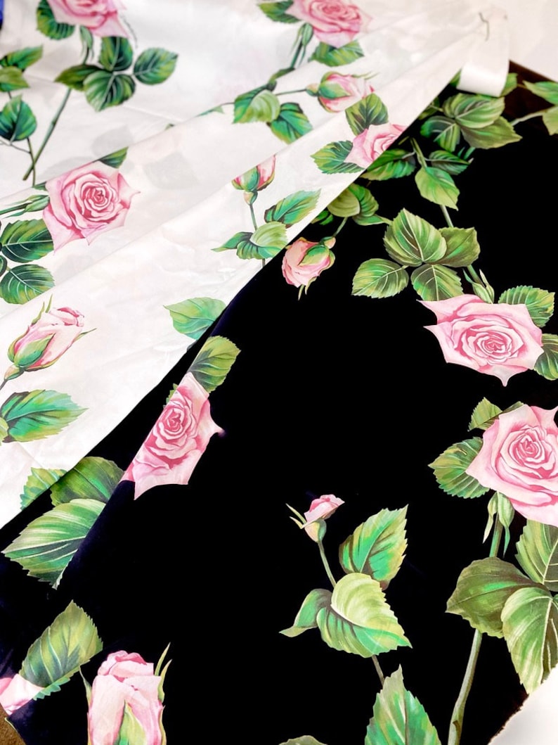May include: Two pieces of fabric with a floral pattern. One piece is white with pink roses and green leaves. The other piece is black with pink roses and green leaves.
