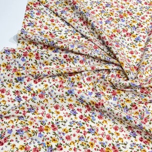 May include: White fabric with a small floral print in shades of pink, yellow, and blue.