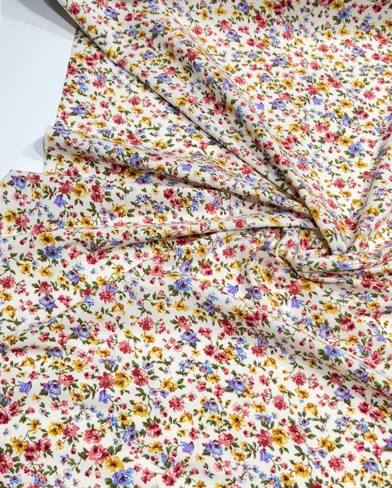 May include: White fabric with a small floral print in shades of pink, yellow, and blue.