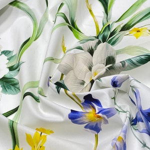 May include: White fabric with a floral print featuring yellow, blue, and white flowers. The fabric has a soft, flowing texture.