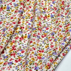 May include: White fabric with a small floral print in shades of pink, yellow, and blue. The fabric is folded in half and the floral pattern is visible on both sides.