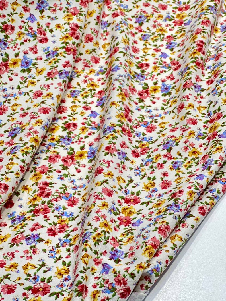 May include: White fabric with a small floral print in shades of pink, yellow, and blue. The fabric is folded in half and the floral pattern is visible on both sides.