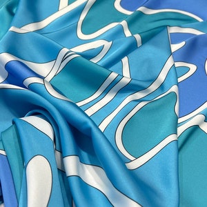 May include: A blue and white patterned silk scarf with a wavy design. The scarf is made of a soft, luxurious fabric and features a variety of shades of blue.