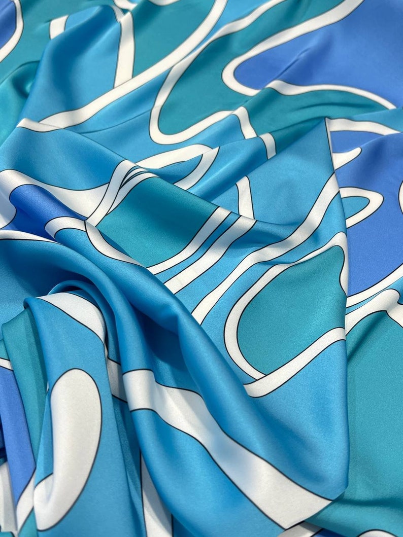 May include: A blue and white patterned silk scarf with a wavy design. The scarf is made of a soft, luxurious fabric and features a variety of shades of blue.