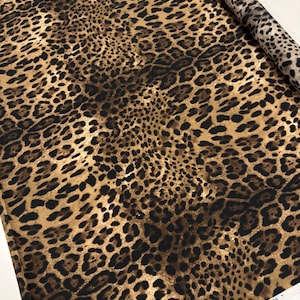 May include: A roll of fabric with a leopard print design. The fabric features a pattern of dark brown spots on a tan and brown background. The fabric is rolled up, showing the pattern on the edge.