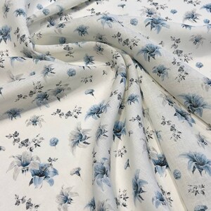 May include: White fabric with a blue floral pattern. The fabric is folded and draped, showing the pattern in detail.