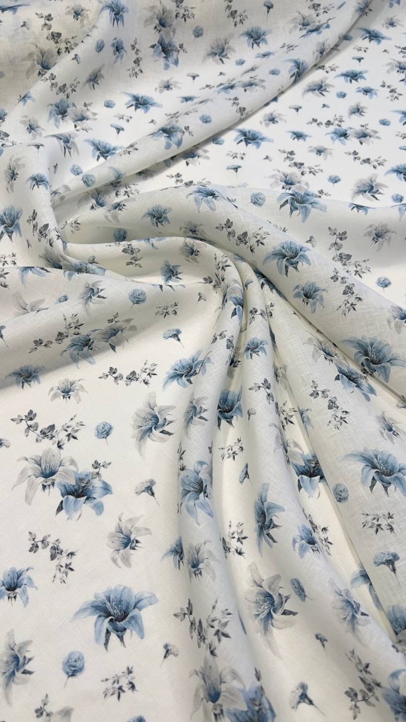 May include: White fabric with a blue floral pattern. The fabric is folded and draped, showing the pattern in detail.