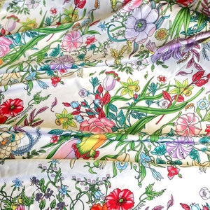 Op de afbeelding: Witte stof met een bloemenprint met verschillende bloemen, bladeren en de tekst "V.ACCORNERO".
