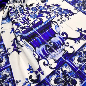 May include: White fabric with a blue and white tile pattern. The pattern features a large blue vase with flowers and intricate designs.