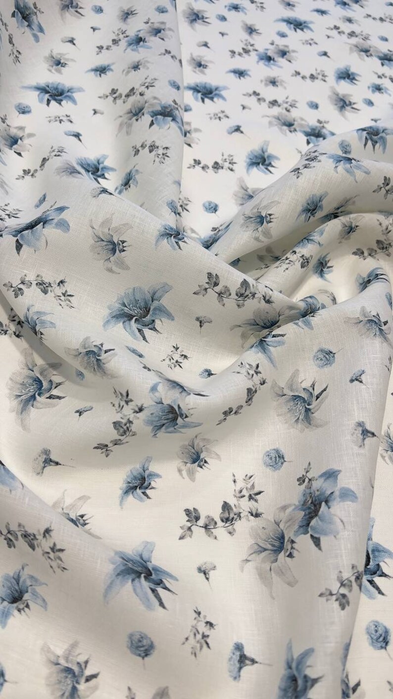 May include: White linen fabric with a blue floral pattern. The fabric is soft and has a subtle sheen.