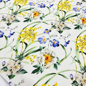 May include: White fabric with a floral print featuring white, yellow, and blue flowers. The flowers are arranged in a repeating pattern.