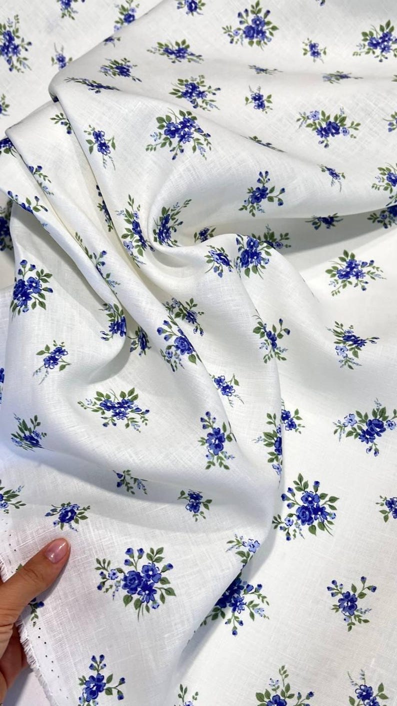 Pu&ograve; includere: Tessuto di lino bianco con un piccolo motivo floreale blu. Il tessuto &egrave; piegato e ha una superficie testurizzata.