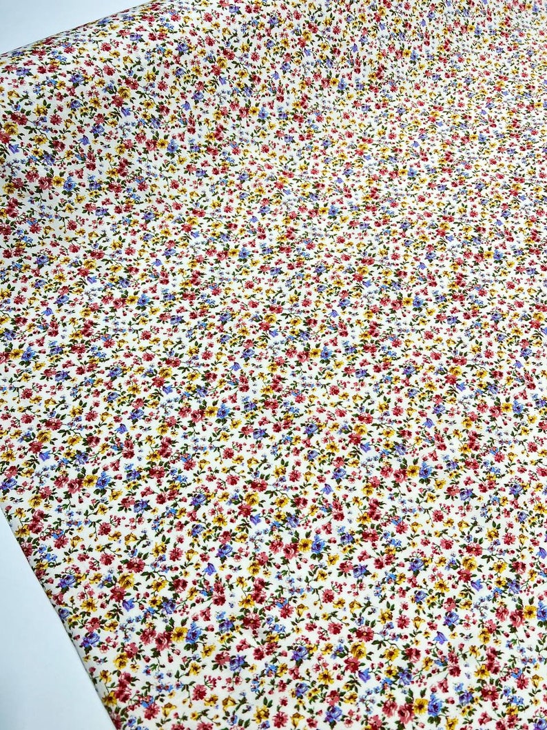 May include: White fabric with a small floral print in shades of red, blue, and yellow.