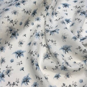 May include: White linen fabric with a blue floral pattern. The fabric is soft and has a subtle texture.