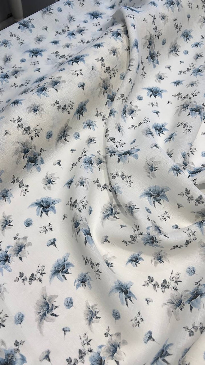 May include: White linen fabric with a blue floral pattern. The fabric is soft and has a subtle texture.