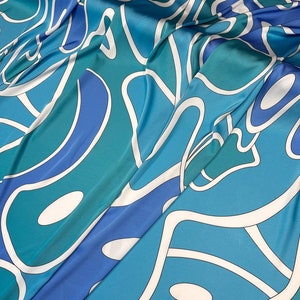 May include: A blue and green fabric with a white abstract pattern. The fabric is folded and has a smooth, silky texture.
