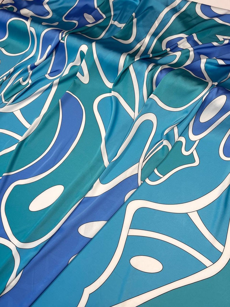 May include: A blue and green fabric with a white abstract pattern. The fabric is folded and has a smooth, silky texture.
