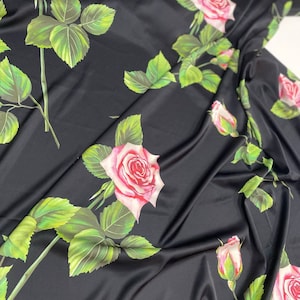 May include: Black satin fabric with a repeating pattern of pink and white roses with green leaves.