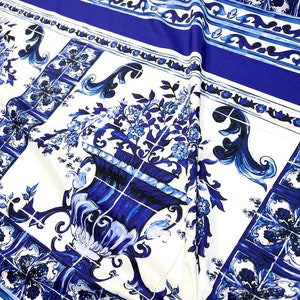 May include: White fabric with a blue and white tile pattern. The pattern features a repeating design of stylized flowers and vases.