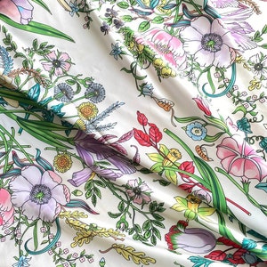 Op de afbeelding: Witte stof met een bloemenprint met verschillende bloemen in roze, paars, geel en groen.