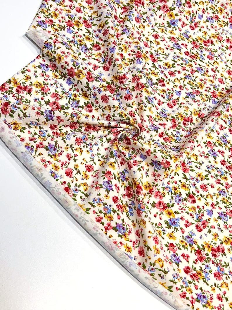May include: White fabric with a small floral print in shades of red, yellow, blue, and green.
