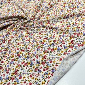 May include: White fabric with a small floral print in shades of red, blue, yellow, and green. The fabric is folded and the underside is visible.