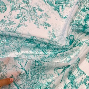May include: White fabric with a teal toile de Jouy design featuring tigers, monkeys, and other animals in a forest setting. The fabric is folded, showing the detailed pattern and texture.