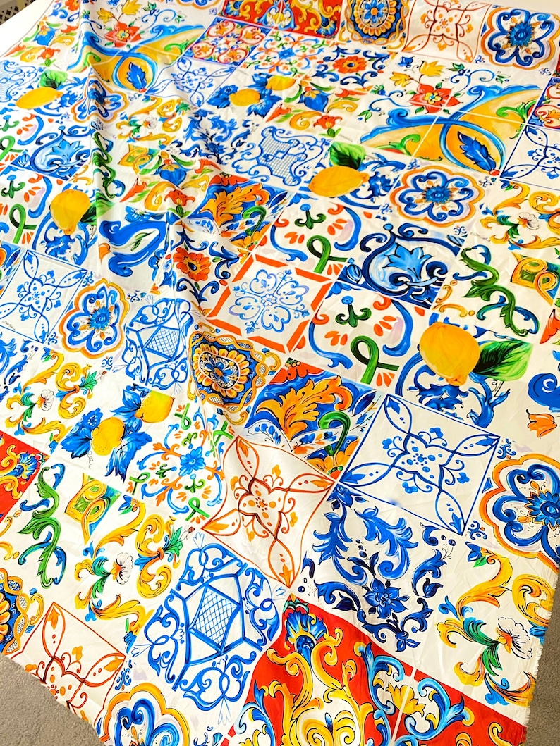 Pu&ograve; includere: Tessuto bianco con un motivo colorato di piastrelle blu, gialle, arancioni e verdi. Le piastrelle presentano disegni floreali e forme geometriche.