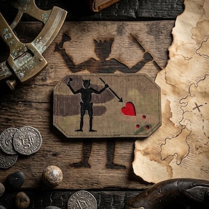 Könnte beinhalten: Ein rechteckiger Aufnäher mit Tarnmuster, der eine schwarze Silhouette einer Piratenfigur zeigt, die einen Speer auf ein rotes Herz richtet, mit drei roten Punkten unter dem Herz, gefertigt aus strapazierfähigem Gewebe.