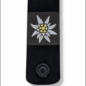 Può includere: Toppa in tessuto nero con un fiore di stella alpina bianco e la parola "Edelweiss" stampata sotto.