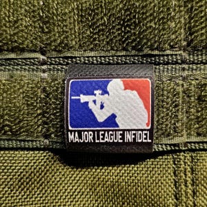 Puede incluir: Parche negro y azul con una silueta blanca de una persona sosteniendo un rifle. El parche tiene el texto "MAJOR LEAGUE INFIDEL" en letras blancas.