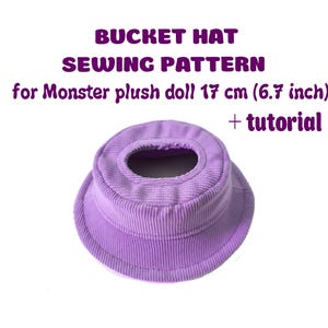 Puede incluir: Un patrón de costura de sombrero de pescador de pana lavanda para una muñeca monstruo de peluche. El sombrero está diseñado para una muñeca de 17 cm e incluye un tutorial. El texto "BUCKET HAT SEWING PATTERN" se muestra en morado.