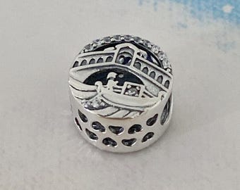May include: Silver charm featuring a detailed depiction of a bridge and gondola in Venice, Italy. The charm is adorned with clear cubic zirconia stones.