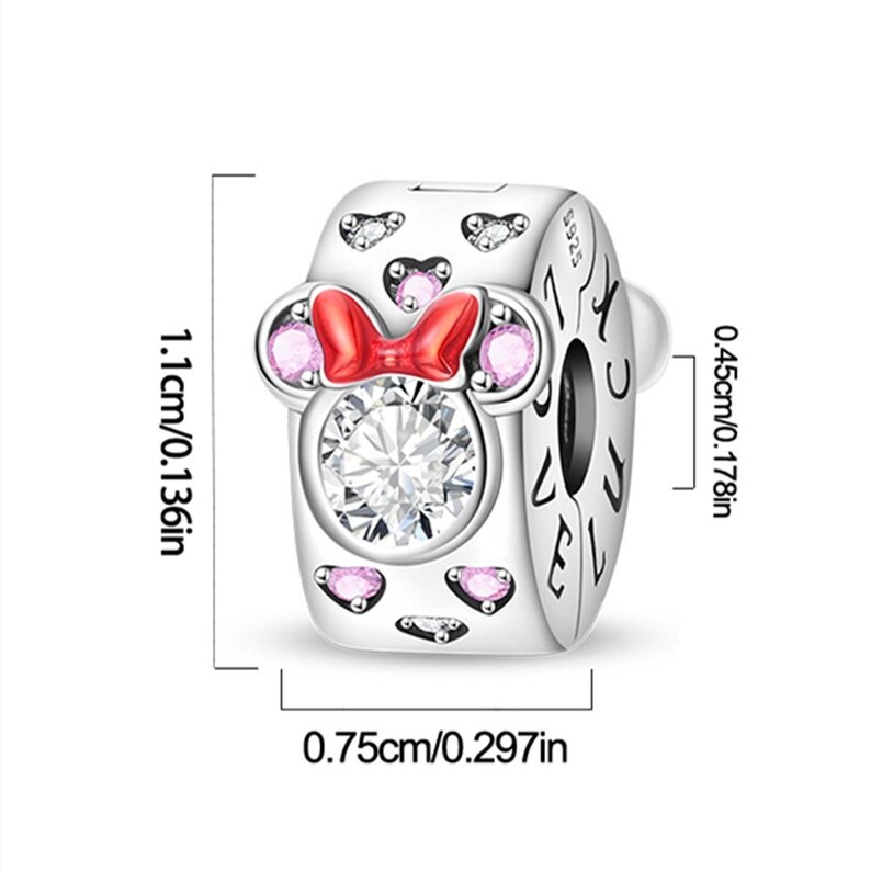 K&ouml;nnte beinhalten: Ein silberner Charm-Anh&auml;nger mit einem zentralen klaren Stein, einer roten Schleife und rosa Steinakzenten in Mausohrform. Die Seite ist mit dem Wort LOVE graviert. Die Ma&szlig;e betragen 1,1 cm x 0,75 cm x 0,45 cm, mit S925-Stempel.