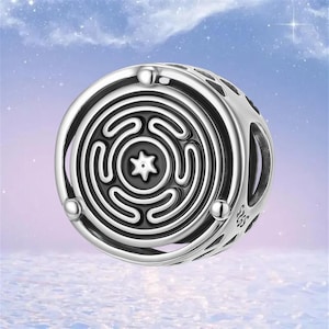 May include: A silver charm with a black and white labyrinth design. The charm has a circular shape with a maze pattern in the center and a star-shaped design. The charm has a polished finish and is likely made of sterling silver.