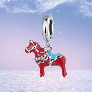 May include: A red horse charm with a blue saddle and rhinestone detailing, suspended from a silver bead. The charm is designed for a bracelet or necklace, with a classic design.