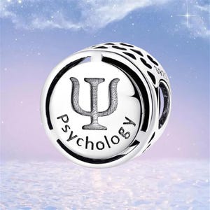 May include: A silver charm featuring the Greek letter psi, the symbol for psychology, and the word "psychology" in a circular design. The charm has a polished finish against a soft, blurred background.