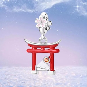 Könnte beinhalten: Ein silberner Charm-Anhänger mit einem roten Torii-Tor, einem weißen Berg und einem funkelnden orangefarbenen Edelstein. Darüber hinaus eine rosa-weiße Kirschblüte. Ideal für ein Armband oder eine Halskette.