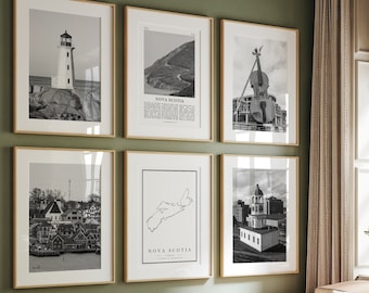 May include: A living room with a green wall and a light brown couch. There are six black and white framed pictures on the wall. The pictures are of a lighthouse, a map of Nova Scotia, a violin, a church, a town, and another map of Nova Scotia. The couch has a green throw pillow and a white and black patterned pillow. There is a small table in front of the couch with a book and a vase with white flowers.