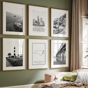 Peut inclure: Un ensemble de six impressions encadrées en noir et blanc représentant différentes scènes de Caroline du Nord. Les impressions comprennent un phare, une carte de l'état, un paysage urbain, un pont et une vue sur la montagne. Les impressions sont disposées en grille sur un mur vert.