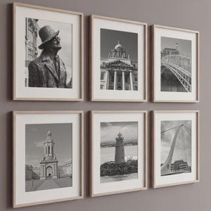 May include: A set of six black and white framed prints arranged in two rows. The images feature various architectural landmarks and a statue, each enclosed in a light wood frame with a white mat, displayed against a solid neutral wall.