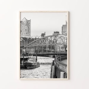 May include: A black and white photograph of a city skyline with a bridge over a river. The bridge is made of metal and has a truss design. There is a boat in the river.