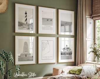 May include: A collection of six framed black and white prints featuring coastal scenes. The prints include images of a lighthouse, beach, and a map of Outer Banks. The frames are gold-colored, and the prints are displayed on a green wall.