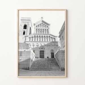 May include: Black and white photograph of a stone building with a large arched doorway and steps leading up to it. The building has a tall tower on the left side and a smaller tower on the right side.