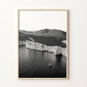 May include: A black and white photograph of a rocky coastline with a small boat in the water. The photo was taken from a high vantage point, giving a panoramic view of the landscape.