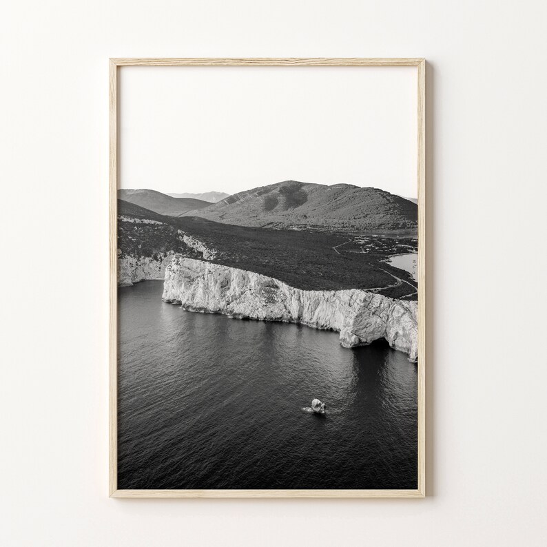 May include: A black and white photograph of a rocky coastline with a small boat in the water. The photo was taken from a high vantage point, giving a panoramic view of the landscape.