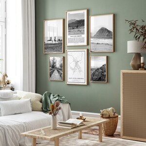 May include: A living room with a white couch and a wooden coffee table. The wall is painted a light green color and has six black and white framed photographs of San Luis Obispo, California. The photographs include a beach scene, a map of the city, and a view of the city from the ocean.